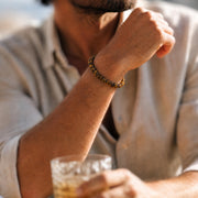 Brown and golden tiger’s-eye disc bead bracelet worn on a man's wrist with a light-colored shirt