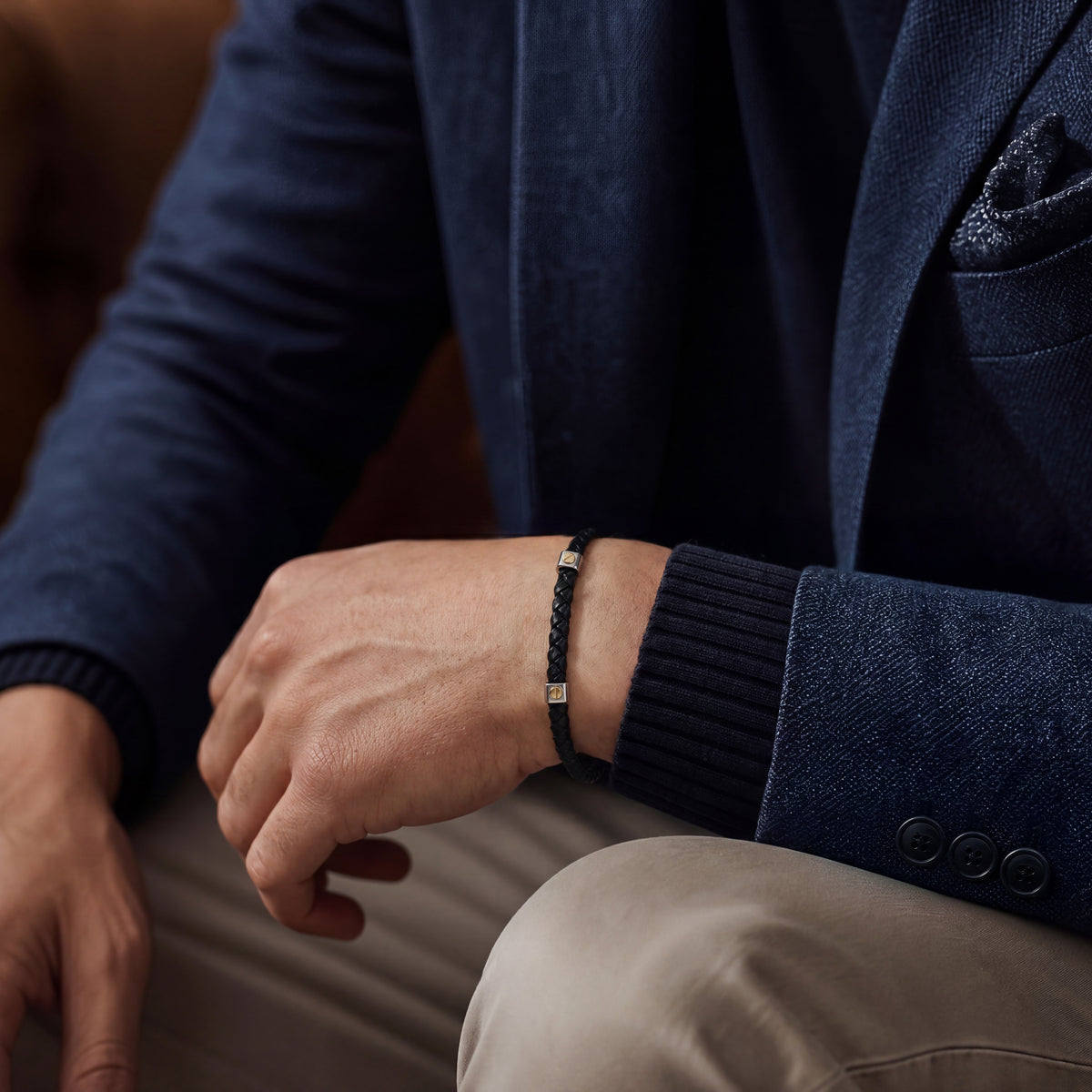 Black braided leather bracelet with silver-tone and gold-tone accents, worn with a navy blazer, men's casual accessory
