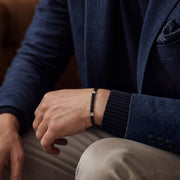 Black braided leather bracelet with silver-tone and gold-tone accents, worn with a navy blazer, men's casual accessory