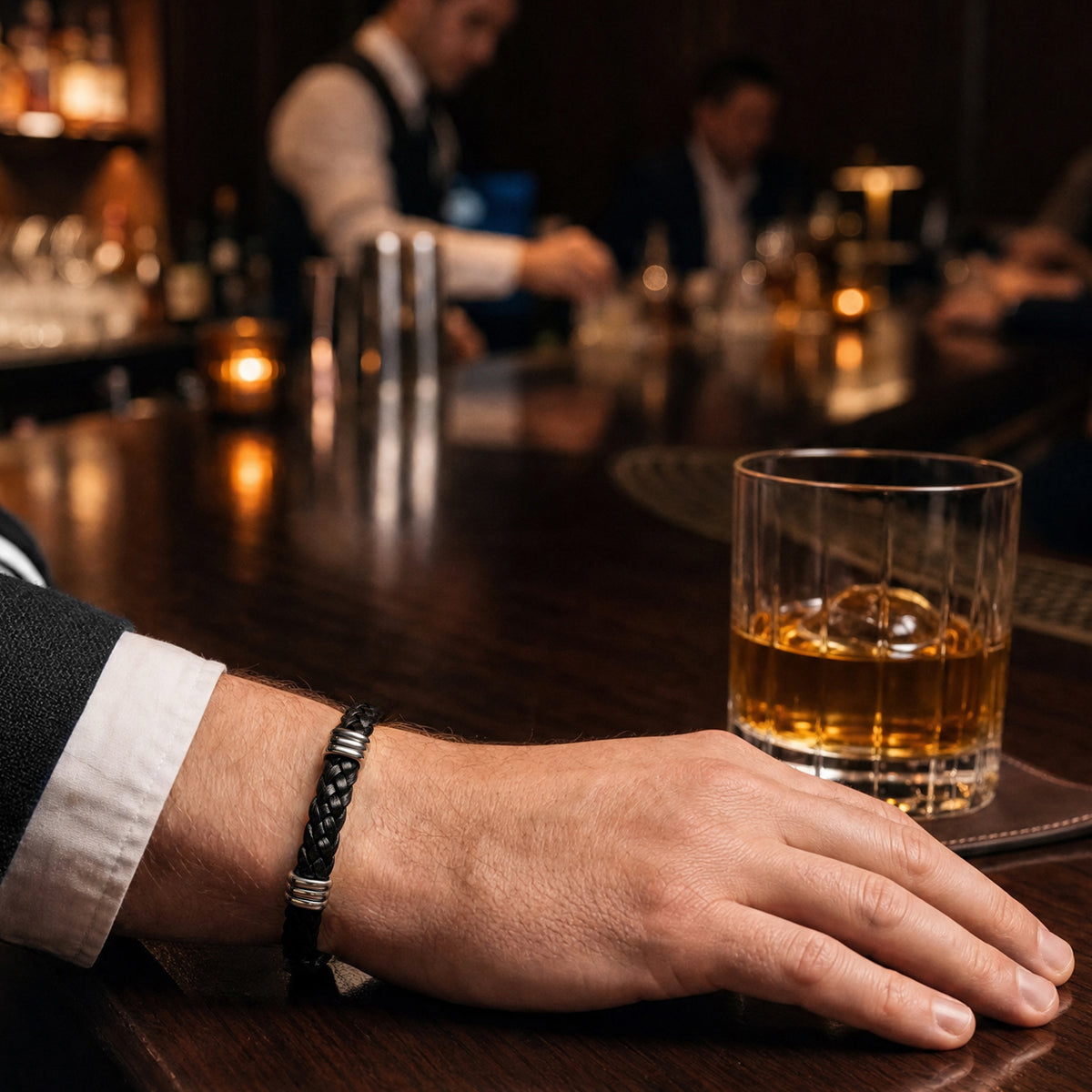  Black braided leather bracelet with silver-tone triple-ring accents worn on a man's wrist at a bar