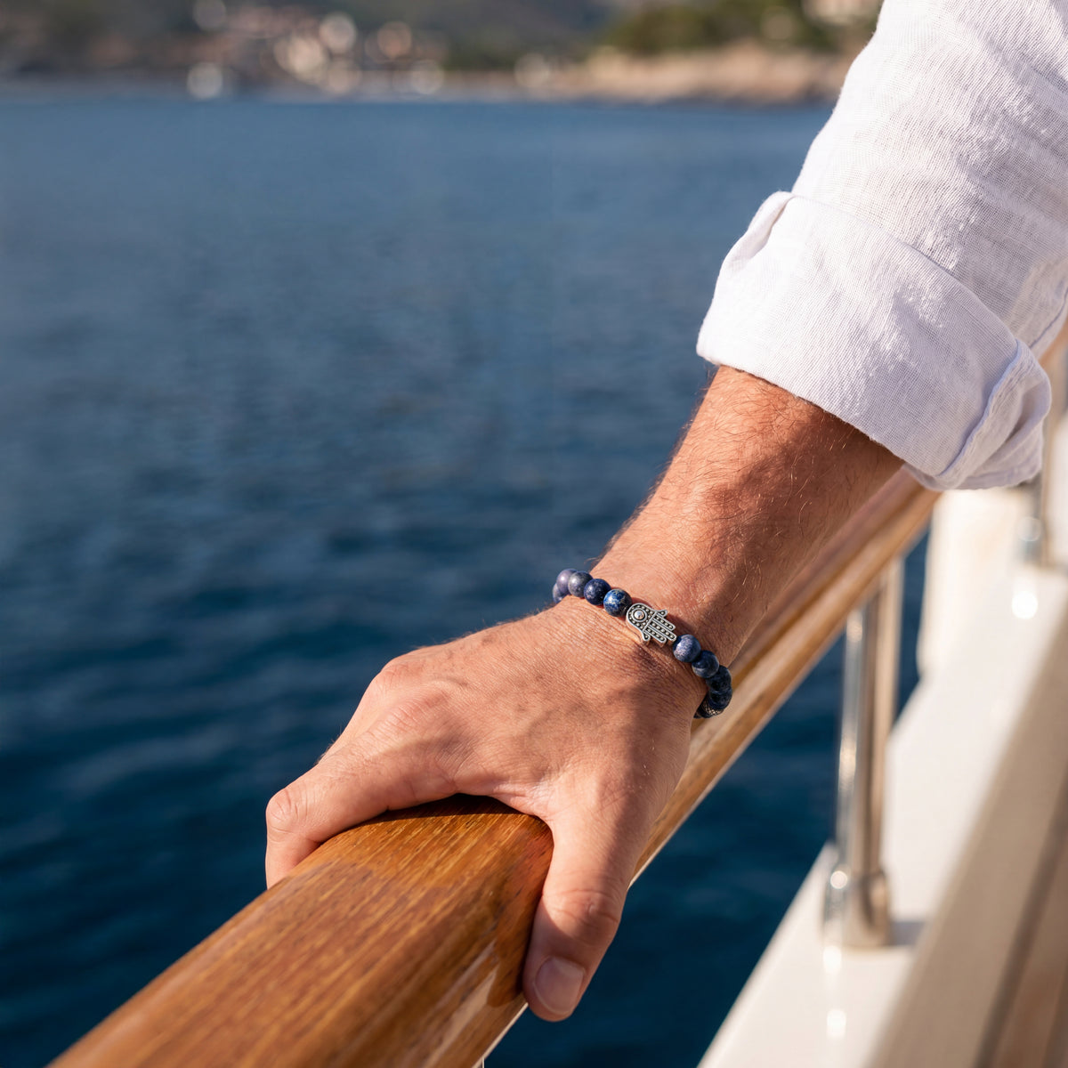  Blue and grey stone bead bracelet with a silver-tone Hamsa hand worn on a man's wrist at a boat railing