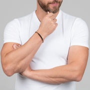 A slim copper-toned twisted cable bracelet with a gunmetal tube bar station worn casually.